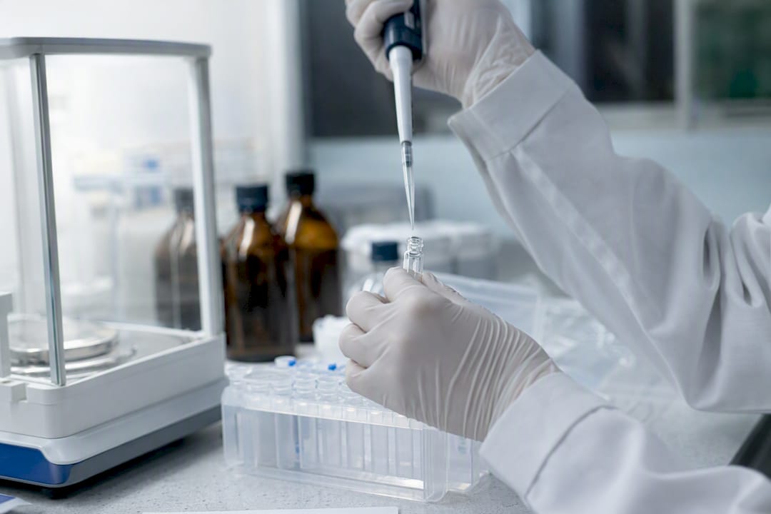 Gloved hands pipetting peptide solution in lab