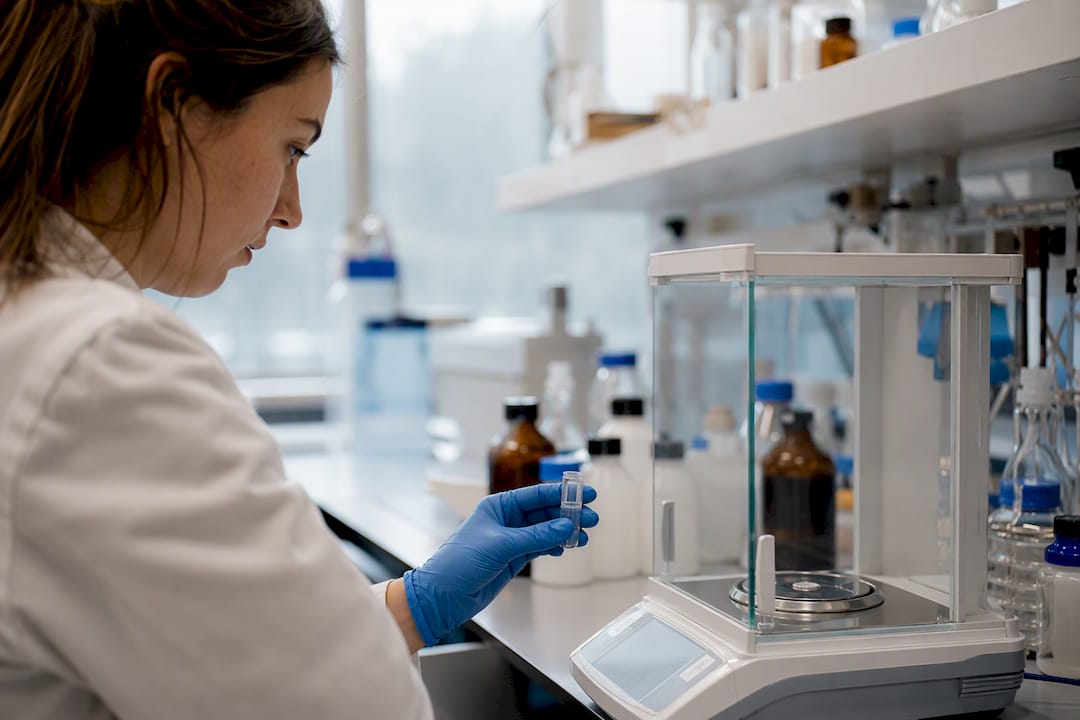 Gloved hand holding sample vial at analytical balance
