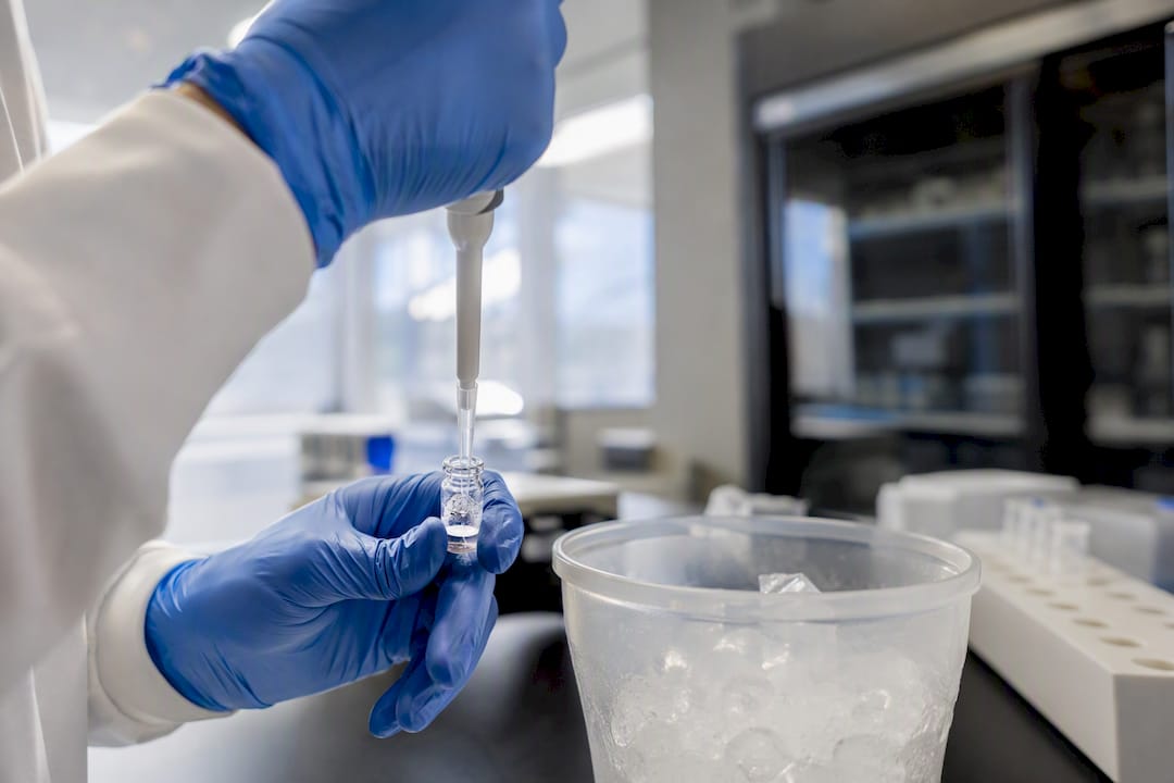 Hands reconstituting peptide vial in lab